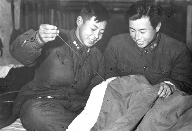 雷鋒(左)在幫助戰友縫被子。新華社發