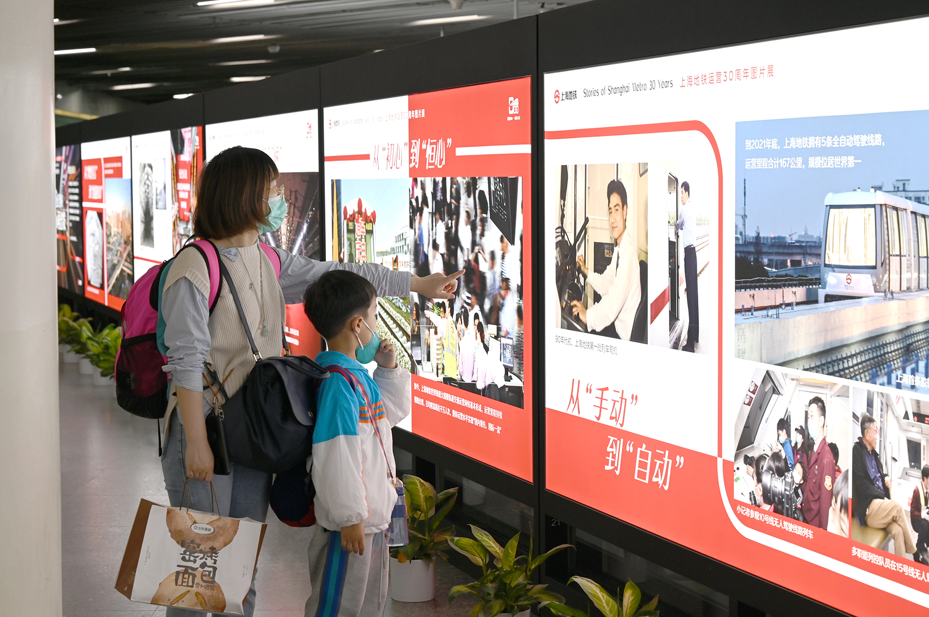 2023年5月25日，上海，地铁人民广场站。一位母亲指着站台里的上海地铁30周年图片展，给孩子讲述三十年前的地铁故事。澎湃新闻记者 吴栋 图