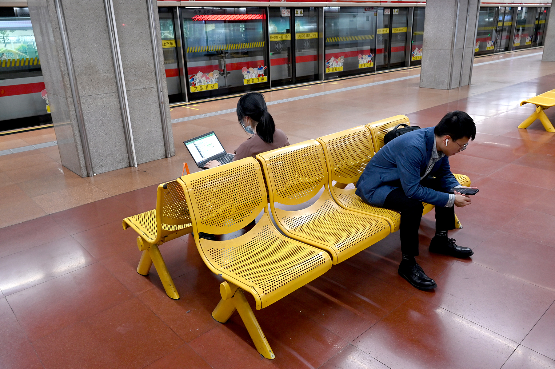 2023年5月25日，上海，地铁上海火车站站。一位正用手提电脑工作的女子与一位等车的男子。澎湃新闻记者 吴栋 图