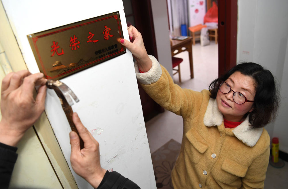 合肥市包河区常青街道工作人员在居民魏松梅(右)家门口悬挂“光荣之家”牌(2019年1月14日摄)。新华社记者 刘军喜 摄