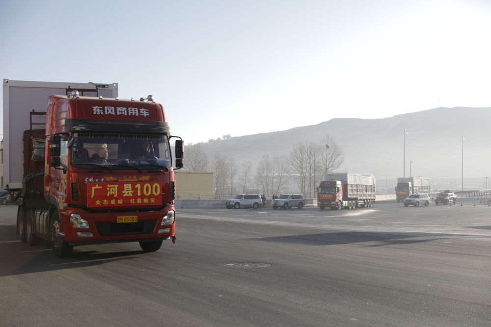 2023年12月26日,在甘肃省临夏州积石山高速出口,载着活动板房的货车驶向受灾乡镇。新华社记者 方欣 摄